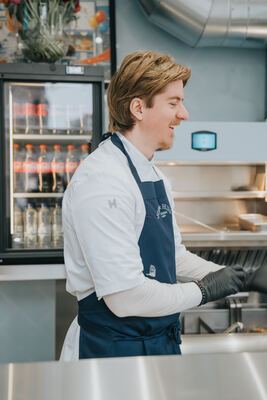 Lachende kok op zij, met het Fish & Fries schort en drankenkoelkast erachter