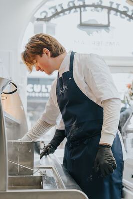 Kok aan het werk bij de frituur, verlicht door het boogvormige etalageraam