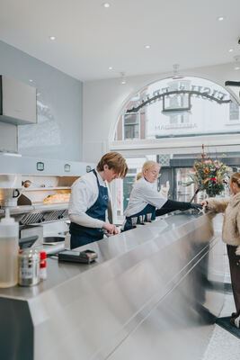 Binnen bij Fish & Fries: strak roestvrijstalen werkblad met beide medewerkers en een klant