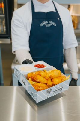 Medewerker presenteert een doos fish and fries op de toonbank, schortlogo zichtbaar